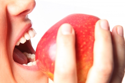 Person's mouth about to bite into a raw red apple.